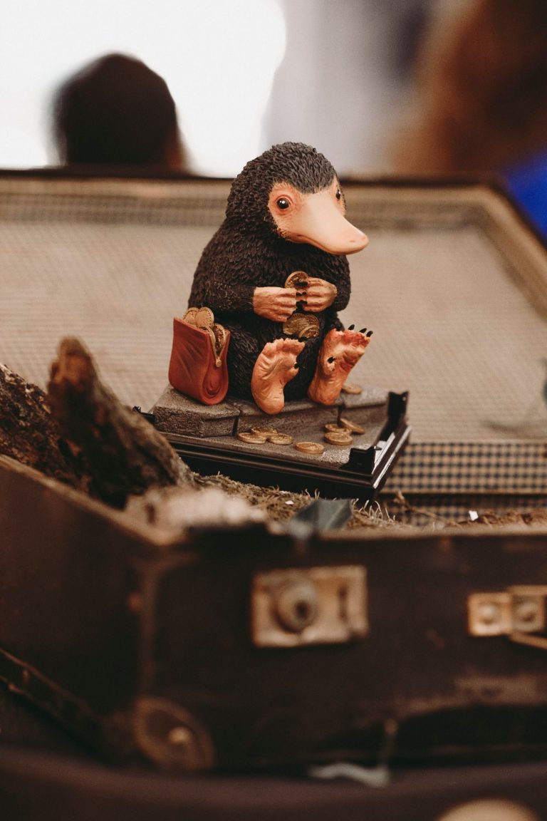 Figurine d'un niffleur assis sur une valise, tenant une pièce dans ses pattes.