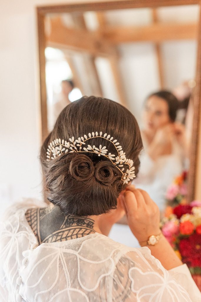 Femme élégante avec un chignon, décorée d'un bijou, se préparant devant un miroir.